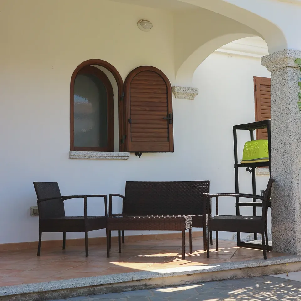 Porticato con finestre ad arco, sedie in rattan e colonna in granito davanti al prato